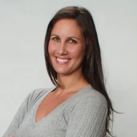 A woman with long hair standing in front of a white wall.